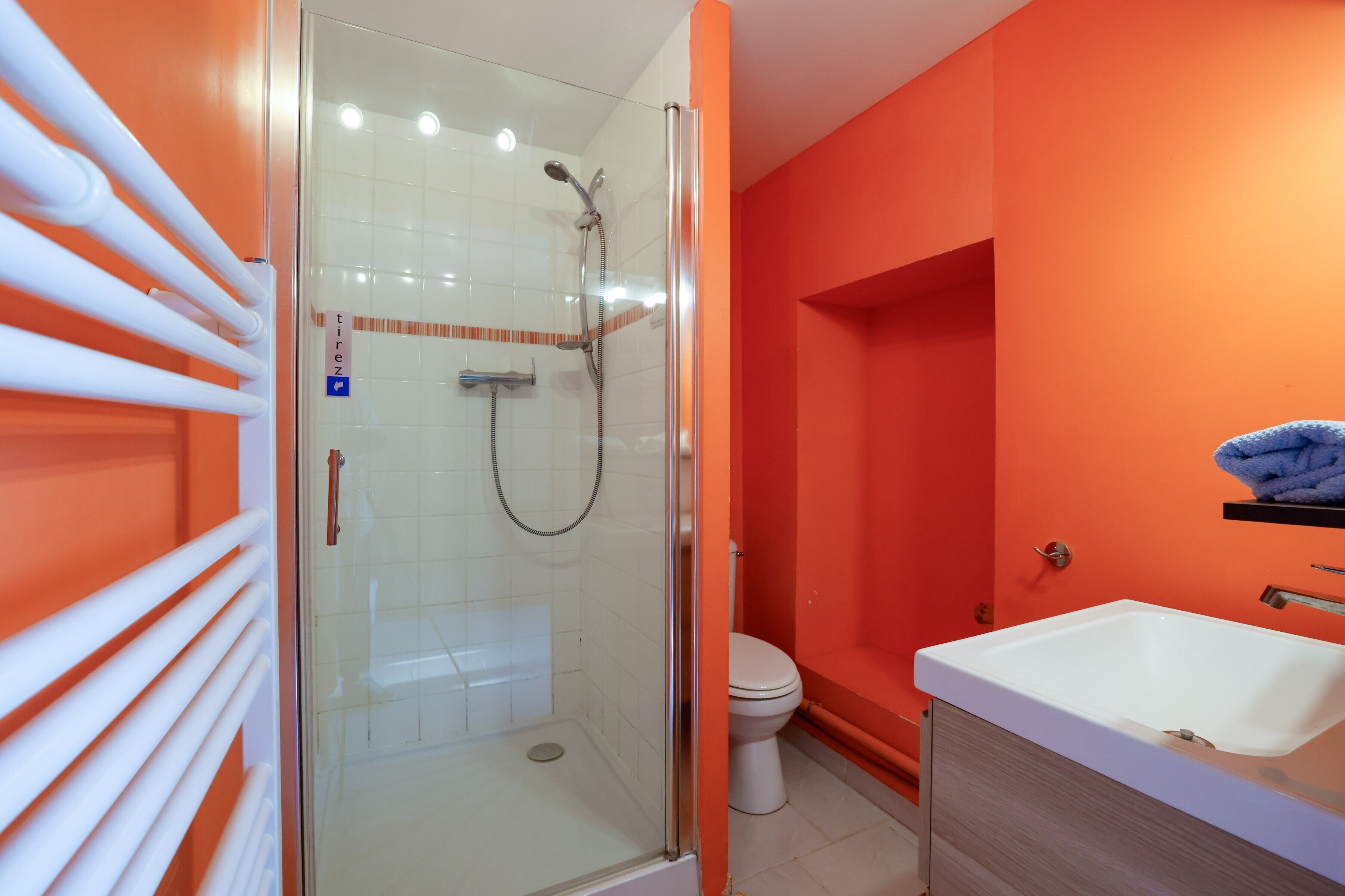 A bathroom with a glass shower enclosure, a white sink, and an orange wall.