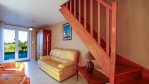 Una sala de estar con una escalera de madera, un sofá amarillo, una mesa de centro de madera y una lámpara.