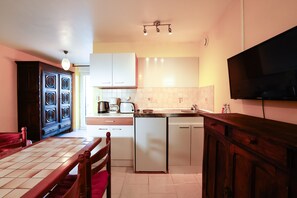 Cocina compacta con una mesa de comedor, un refrigerador, un microondas y un televisor montado en la pared.