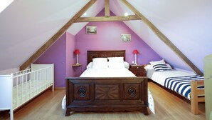 Un dormitorio con techo inclinado, estructura de cama de madera, dos mesitas de noche, una cuna y una estantería fijada a la pared.
