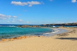 A beach with clear blue water, sandy shore, and rocky outcrops.
