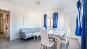 A modern room with a dining table, chairs, a sofa, and a window with curtains. - Apartment 'Apartamento Los Hermanos' with Wi-Fi and Air Conditioning (Es Pujols)