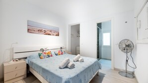 A bedroom with a bed, bedside table, wall art, and a standing fan. - Apartment 'Apartamento Los Hermanos' with Wi-Fi and Air Conditioning (Es Pujols)