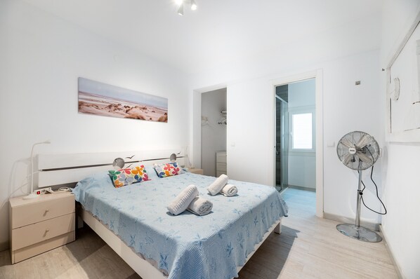 A bedroom with a bed, bedside table, wall art, and a standing fan.