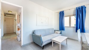 A room with a light blue sofa, a white table, and a window with blue curtains. - Apartment 'Apartamento Los Hermanos' with Wi-Fi and Air Conditioning (Es Pujols)