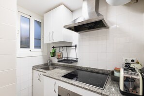 Cucina con pensili bianchi, cappa in acciaio inossidabile, lavello a due vasche, piano cottura integrato e un tostapane.