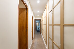 Un corridoio con porte in legno, pavimento piastrellato e vista su una stanza con tavolo e sedia.