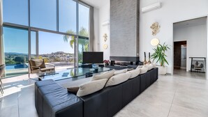 Ett modernt vardagsrum med ett stort glasbord, en svart soffa och en platt-TV.