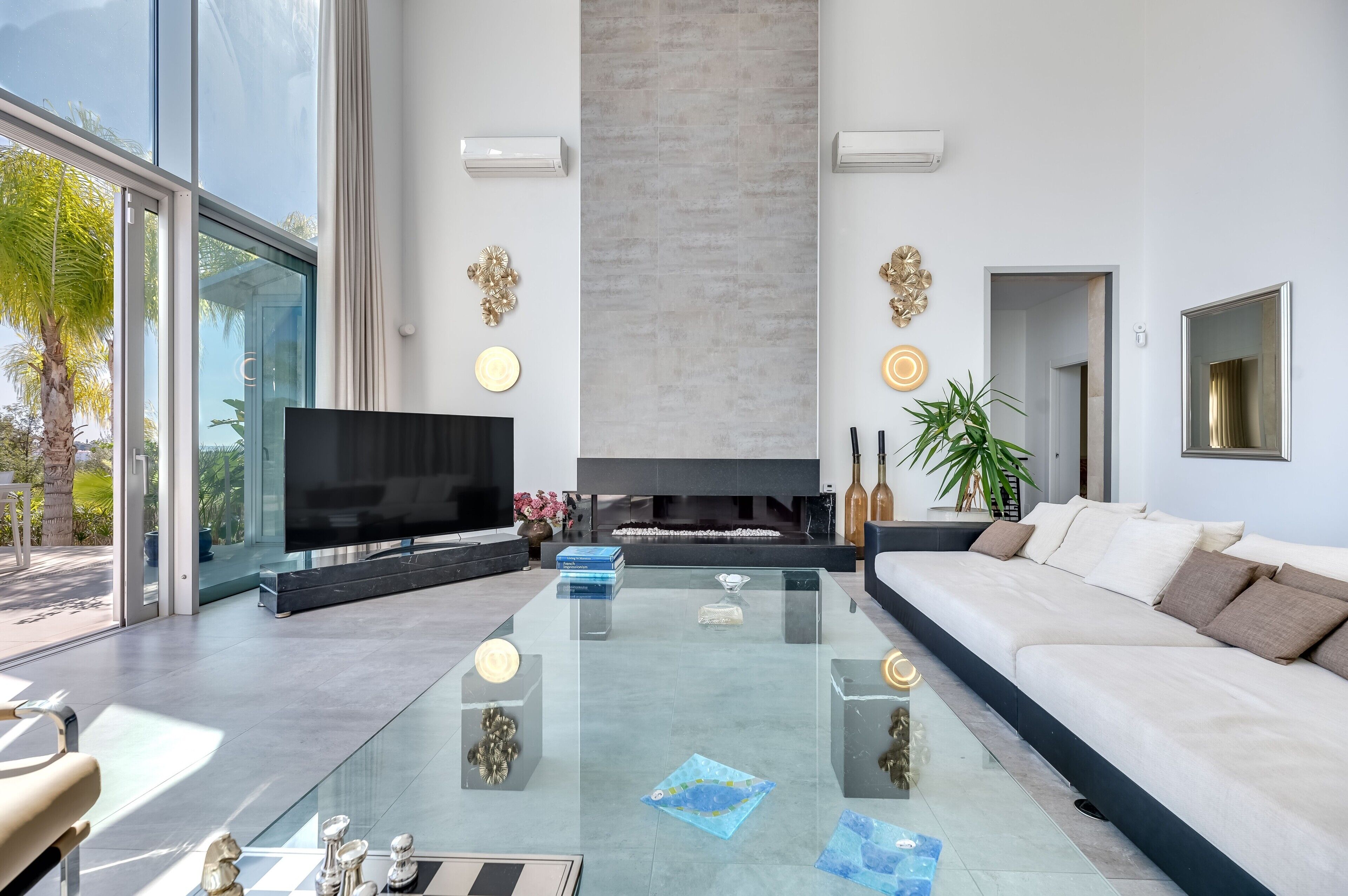 Una sala de estar moderna con un televisor de pantalla plana grande, una mesa de centro de vidrio, un sofá blanco y una chimenea.