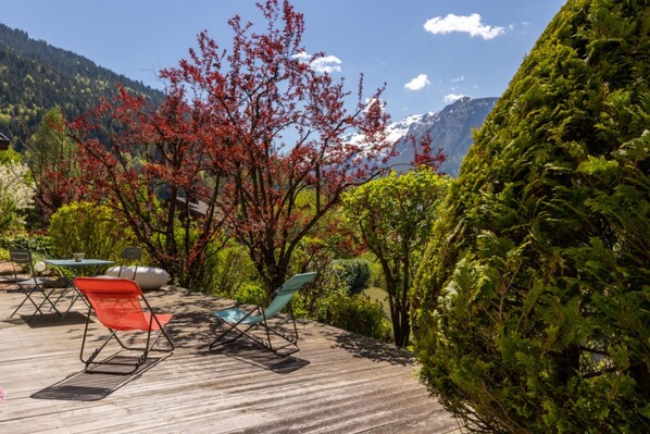 A deck with chairs, a table, and a view of mountains and trees.