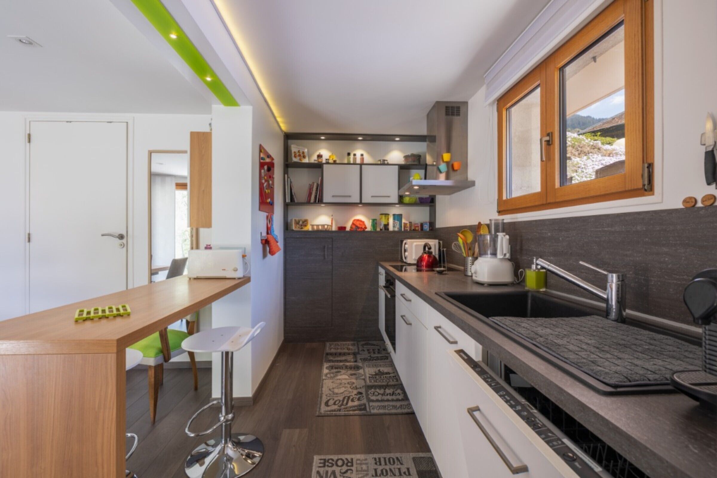 A modern kitchen with a wooden bar counter, white cabinets, and a built-in dishwasher.
