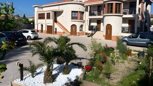 A multi-story residential building with a curved roof, balconies, and a driveway with parked cars.