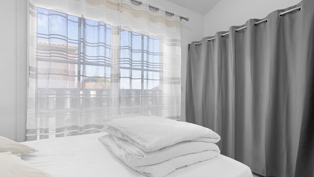 A bedroom with a bed, curtains, and a window.