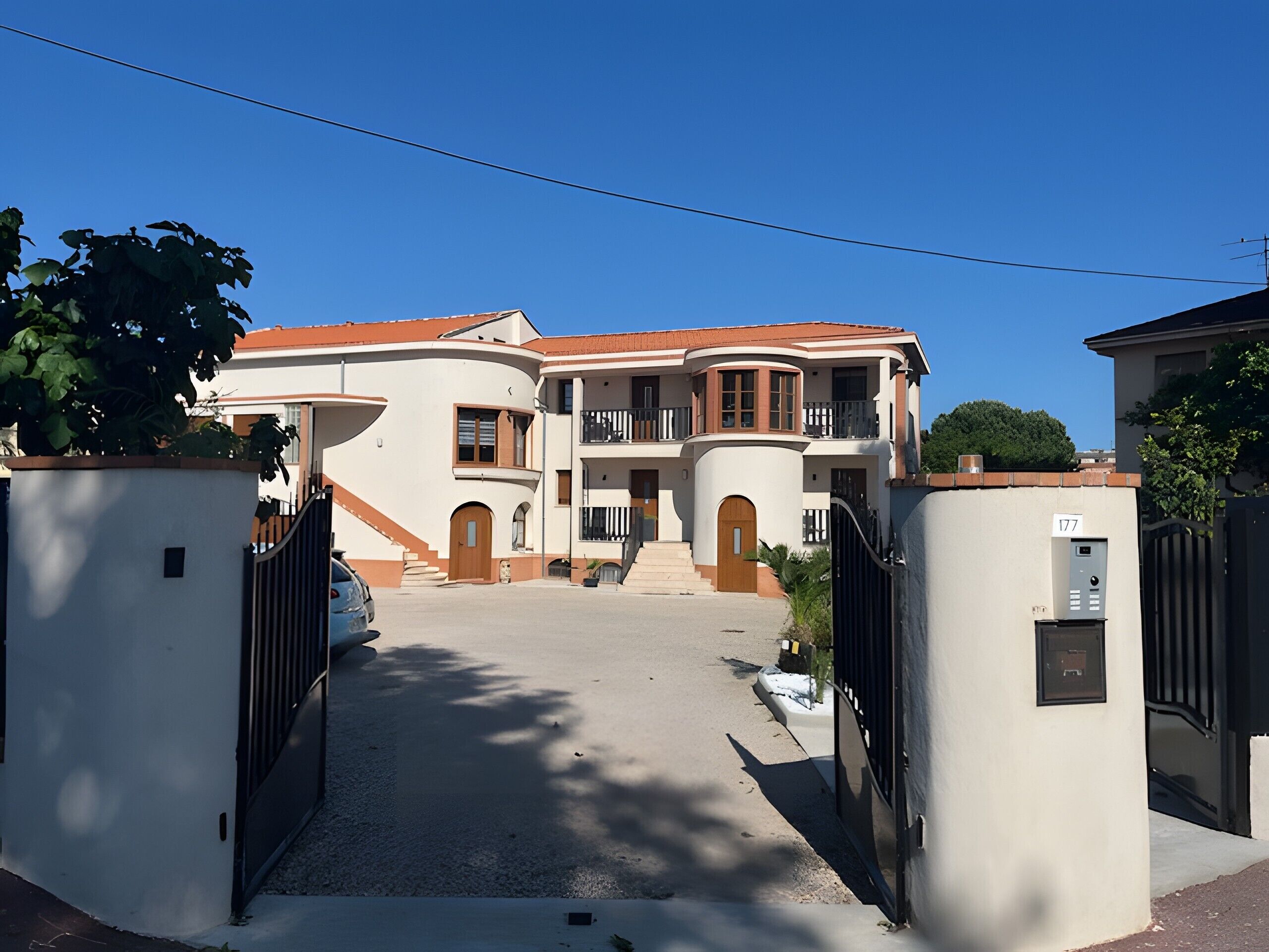 A large, multi-story building with a central entrance, balconies, and a gated driveway.