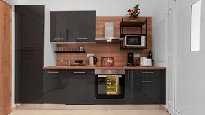 A modern kitchen with black cabinets, a microwave, a coffee maker, and a wooden shelf.