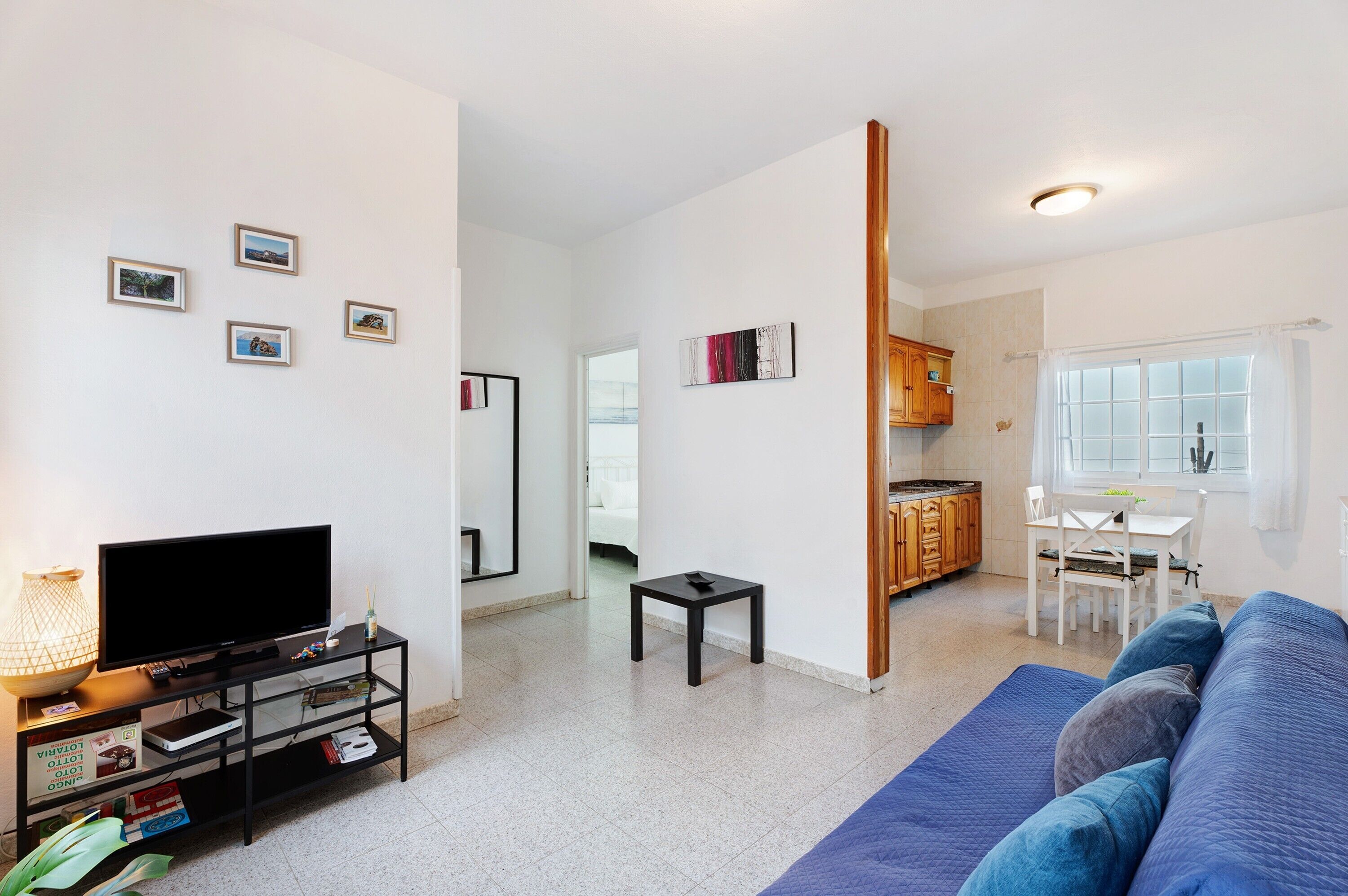A living room with a TV, a small table, a sofa, and a kitchen area with a dining table and chairs.