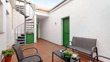 Une cour intérieure avec un escalier en colimaçon, une porte verte, un banc et une table agrémentée d’une plante.