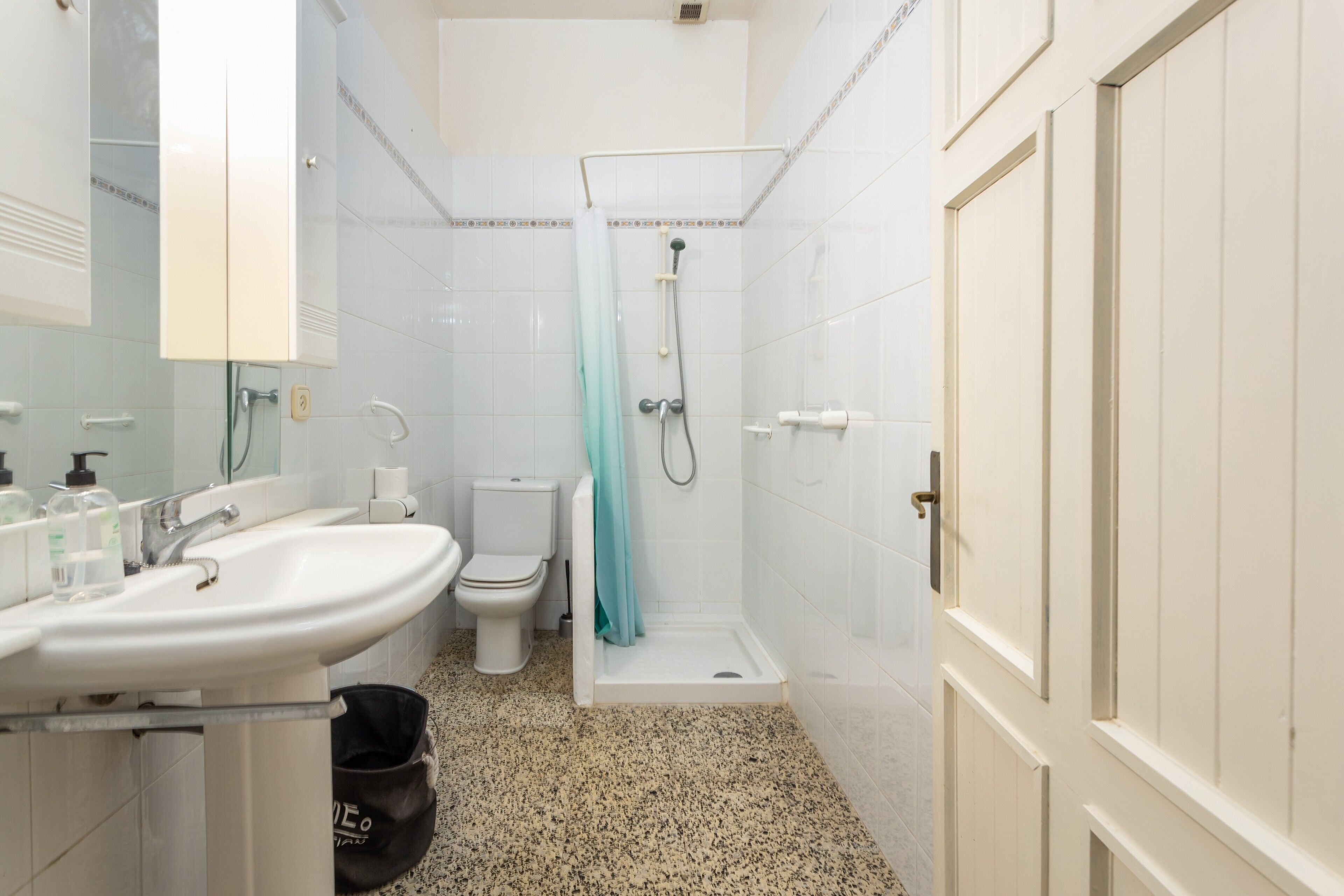 A bathroom with a sink, toilet, shower, and a door.