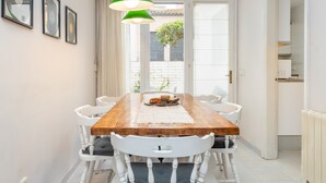 Ein Essbereich mit Holztisch, weißen Stühlen, einer grünen Pendelleuchte und gerahmten Bildern an der Wand.