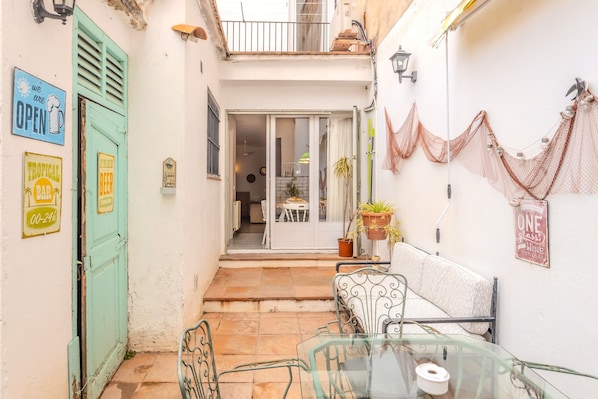 Une petite cour avec une table en verre, des chaises, un canapé et une porte sur laquelle est inscrit « OUVERT ».