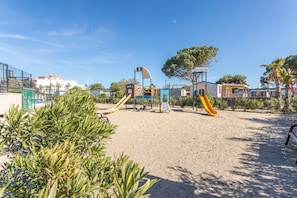 Een speeltuin met glijbanen en klimconstructies, omringd door zand en groen.