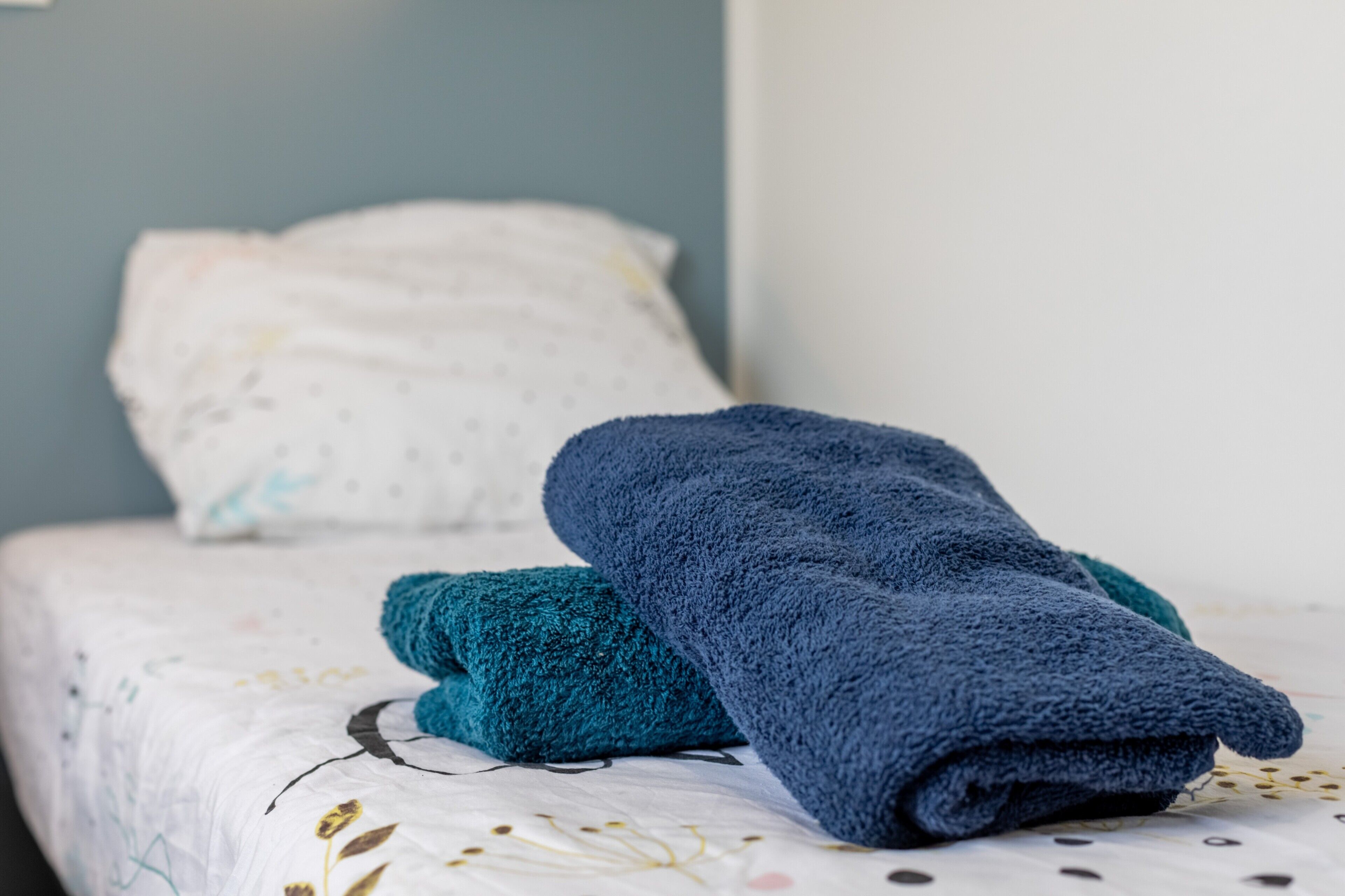 Una cama con una colcha blanca y una toalla azul.