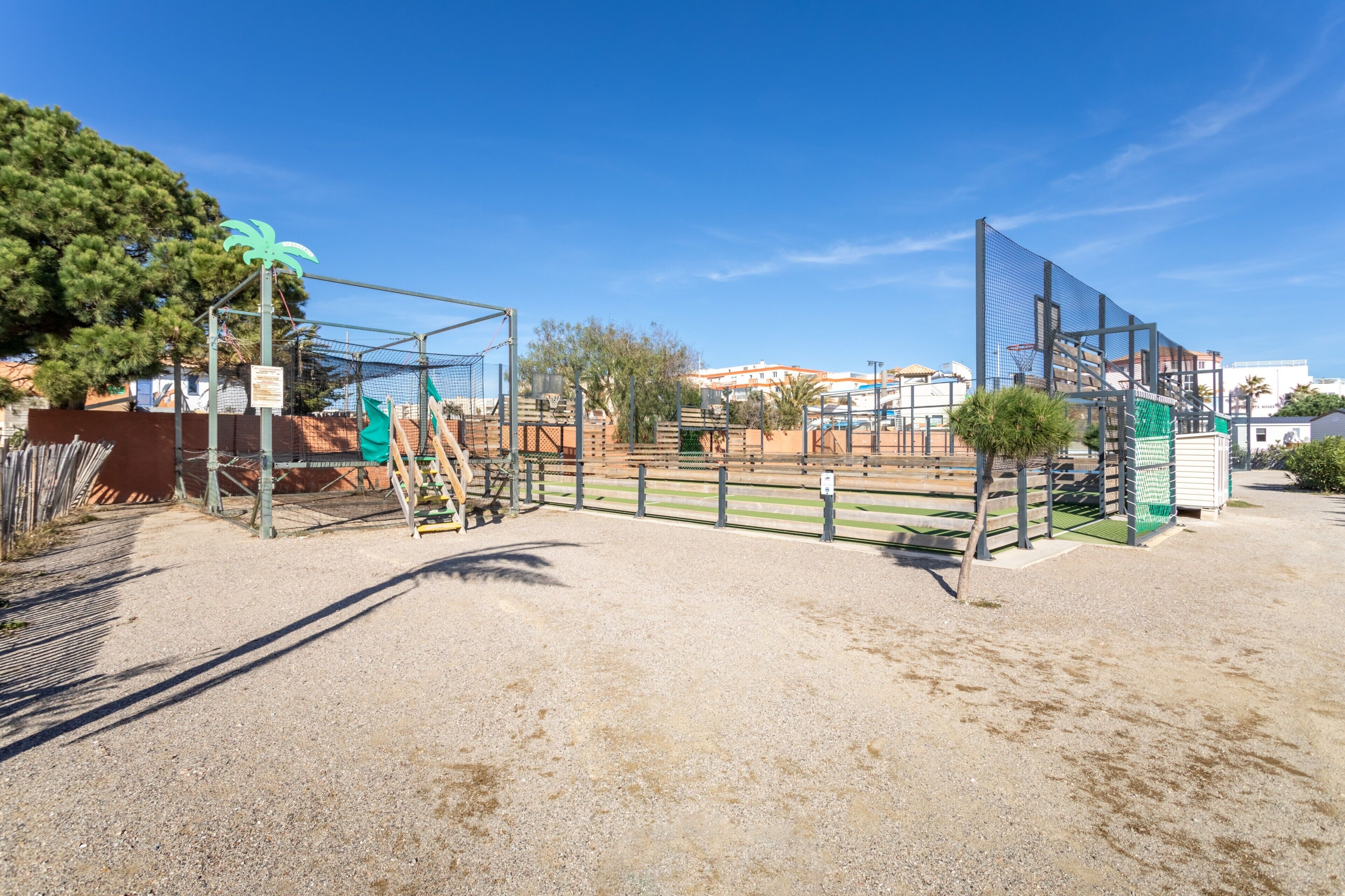 An outdoor equestrian arena with fencing, a palm tree, and a building in the background.