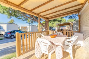 Overdekt terras met tafel en stoelen, een houten terras en zicht op stacaravans op de achtergrond.