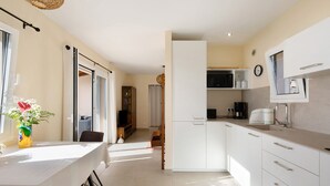 A modern kitchen with white cabinets, a dining table, and a view to a balcony. - Vacation Home "Casa Inti" with Sea View, Private Garden & Wi-Fi (Tijarafe)