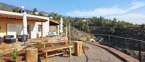 A patio with outdoor furniture, a wooden bench, and a view of a hillside.