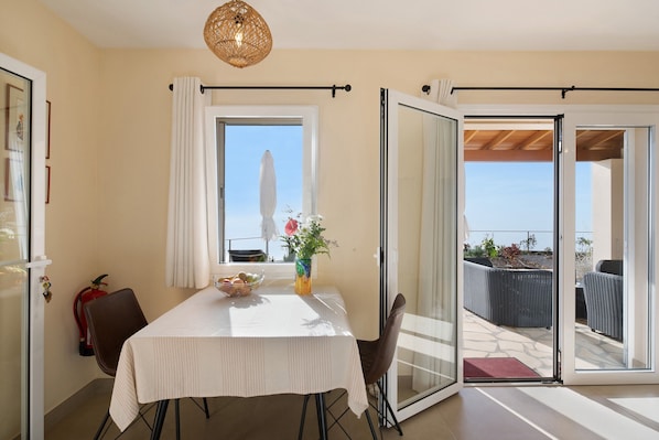 Un espace repas comprenant une table, des chaises, un vase avec des fleurs et une vue sur l’extérieur grâce à une porte coulissante.