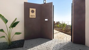 A modern building entrance with a sign reading 'INTI' and a sun symbol, surrounded by a paved area and a plant. - Vacation Home "Casa Inti" with Sea View, Private Garden & Wi-Fi (Tijarafe)