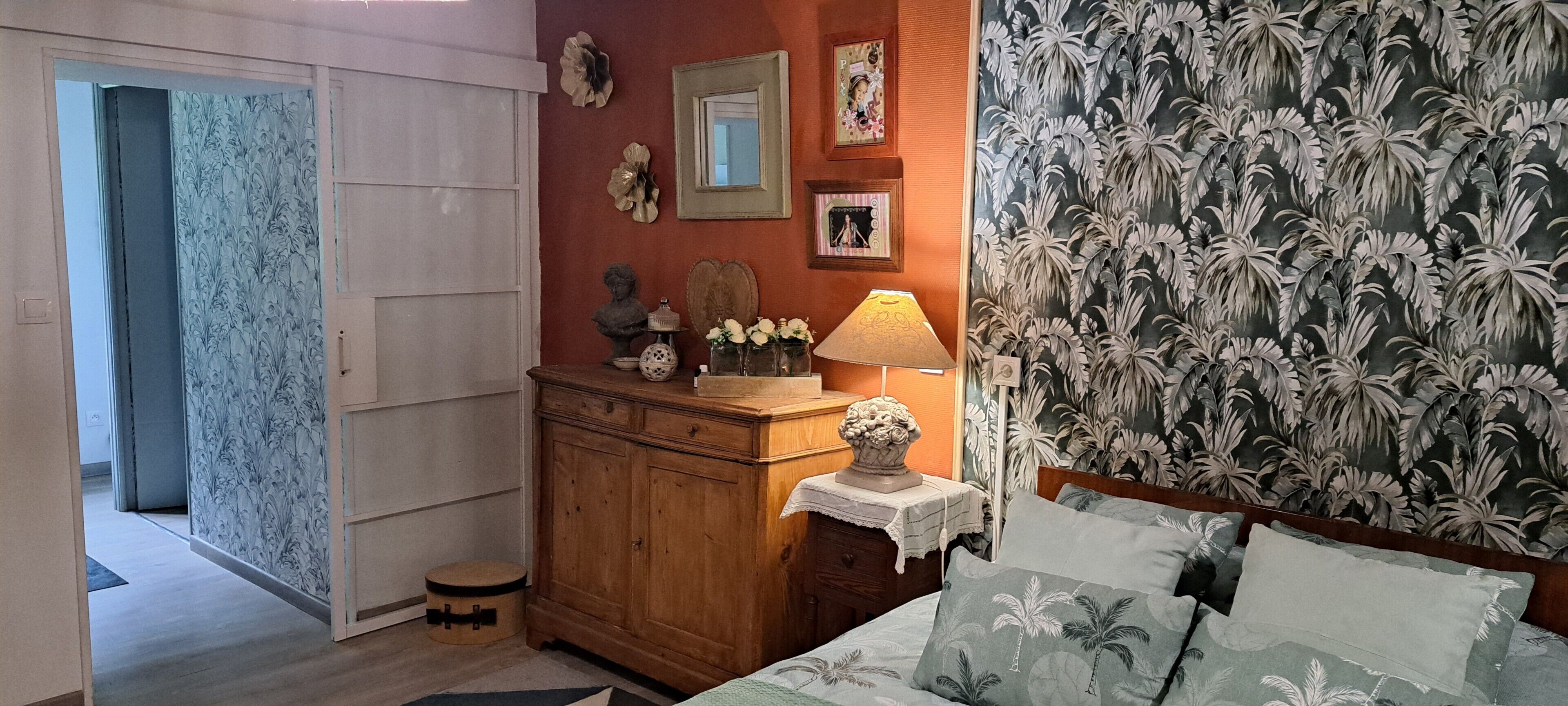 A bedroom with a bed, a nightstand, a dresser, and a wall with floral wallpaper.