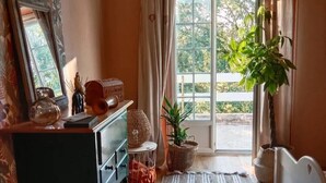 Ein Zimmer mit Holzboden, einem Schreibtisch mit Schubladen, einem Stuhl, einem großen Fenster mit Vorhängen und einem Blumentopf.