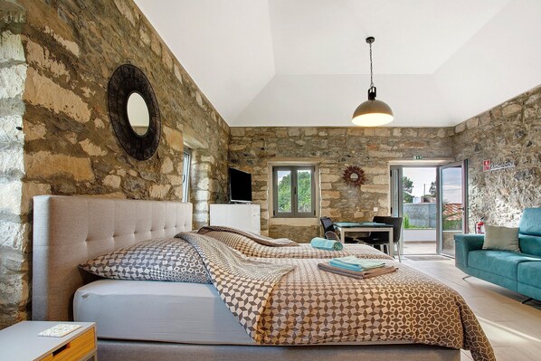 Un dormitorio con pared de piedra, una cama con ropa de cama estampada, un escritorio y un sofá azul.