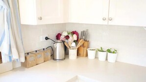 A kitchen with white cabinets, a kettle, wooden spice containers, a knife set, and potted plants. - Fair Linden's Morrow (Bowral)