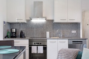 A modern kitchen with white cabinets, a stainless steel range, a coffee maker, and a dishwasher.