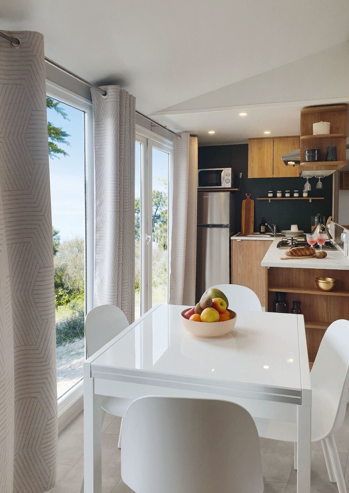 A modern kitchen with a dining area, large windows, and a view of the outdoors.