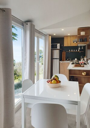 A modern kitchen with a dining area, large windows, and a view of the outdoors.