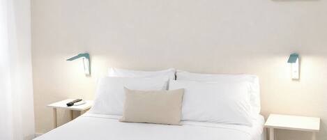 Una habitación de hotel con cama, mesitas de noche, un equipo de aire acondicionado y cuadros colgados en la pared.
