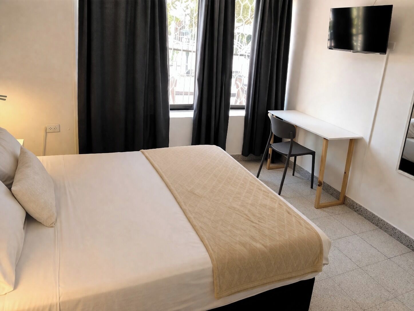 Ein Hotelzimmer mit einem Bett, einem Schreibtisch, einem Sessel, einem an der Wand befestigten Fernseher und einem Fenster mit Vorhängen.
