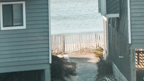 A narrow pathway leading to a beach, flanked by two buildings with balconies and a wooden fence. - Port of Call~2BR~Sleeps 10~Dogs ok~Steps to beach (Port St. Joe)