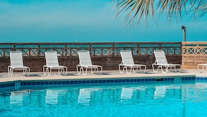 A swimming pool with four white lounge chairs and a wooden fence in the background. - Port of Call~2BR~Sleeps 10~Dogs ok~Steps to beach (Port St. Joe)