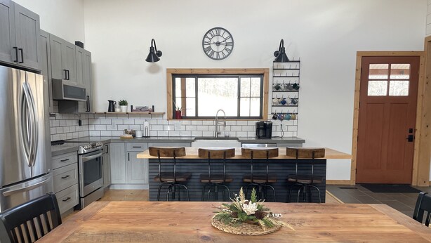 A modern kitchen with grey cabinets, a stainless steel refrigerator, a microwave, and a wooden dining table with chairs. - Bluebird Hill - rolling hills, meadows, large deck, fire pit, 3 bedroom, 2 bath (Guysville)