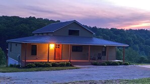 A two-story wooden cabin with a porch, a front door, and a small window on the upper floor. - Bluebird Hill - rolling hills, meadows, large deck, fire pit, 3 bedroom, 2 bath (Guysville)