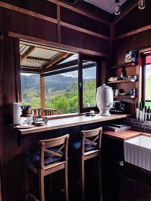 A rustic kitchen with wooden walls and a large window overlooking a green landscape.