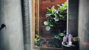 A modern bathroom with a glass door leading to a garden, tiled walls, and a small round table with toiletries. - Grey Gum Luxury Cottage & Highland Cows (Mount Pleasant)