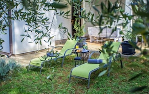 Eine Terrasse mit zwei grünen Liegestühlen, einem kleinen Tisch mit einem Getränk und einem Blumentopf.