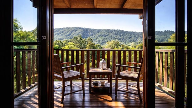 Une terrasse en bois avec deux chaises et une table, donnant sur une colline boisée.