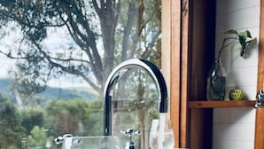 Une personne tenant un verre d’eau près d’un lavabo de salle de bain où l’eau coule.
